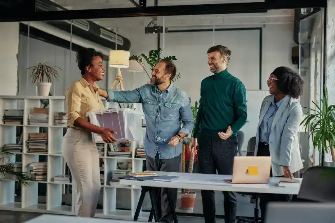Colleagues warmly welcoming a woman back to the office, returning to work in sales.